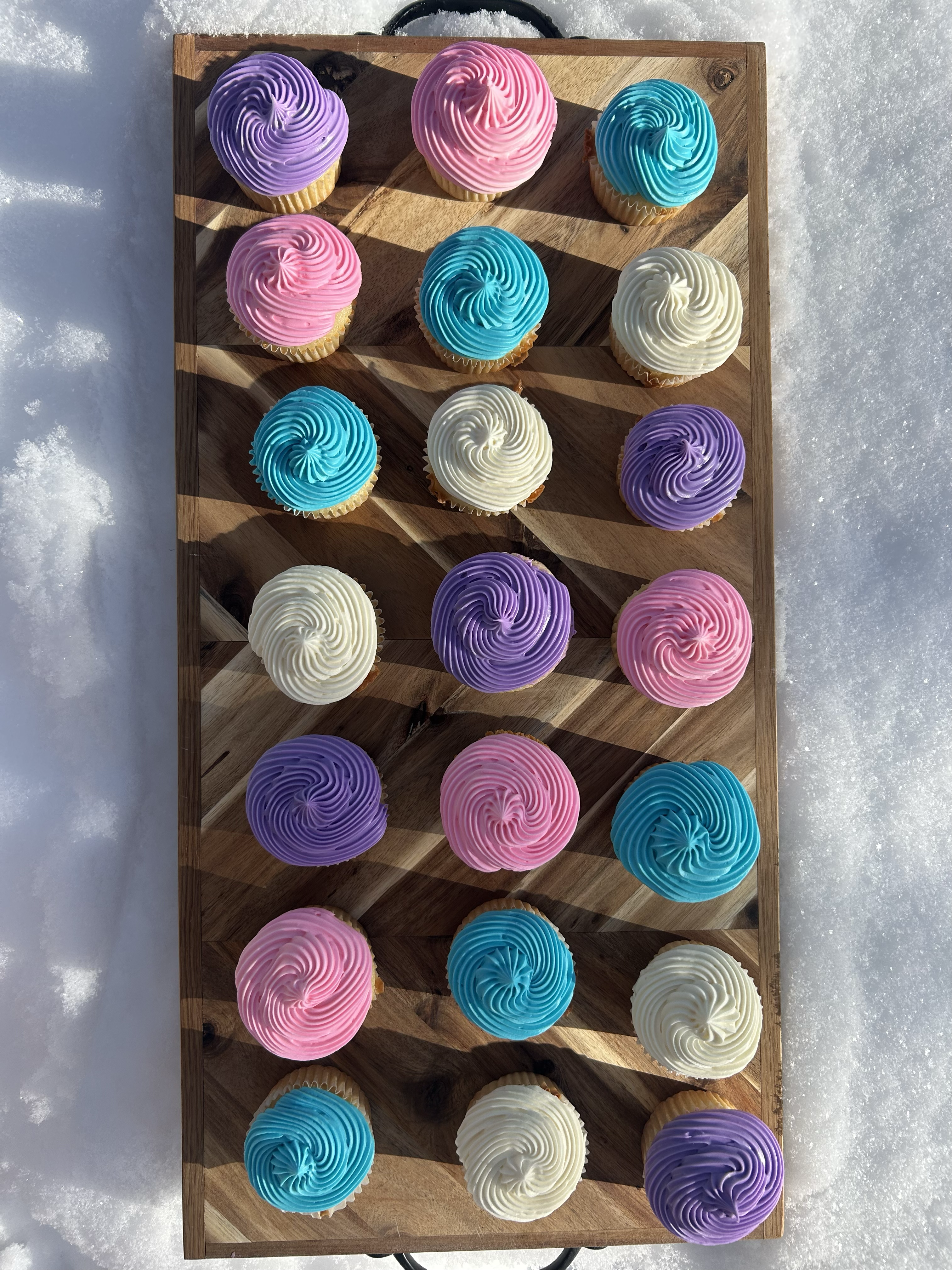 Colorful cupcakes displayed on wooden board in snow